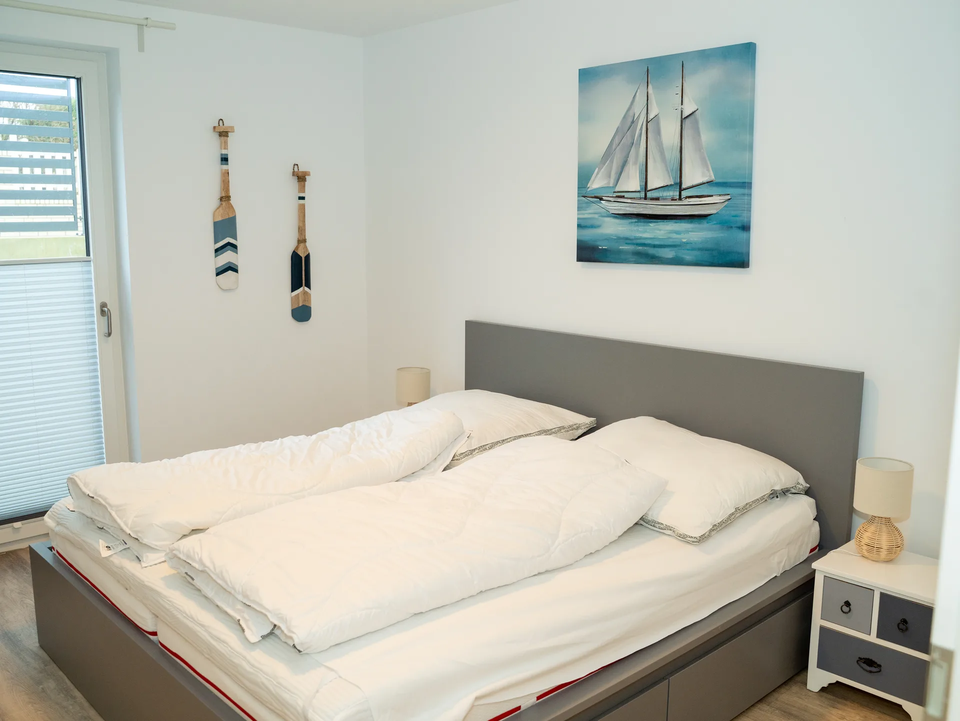 Maritim dekoriertes Schlafzimmer mit Doppelbett und Segelschiff-Gemälde in der Ferienwohnung Kurparkperle
